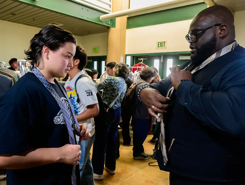 DJ Criner teaching a student how to tie a tie at the Suit Drive